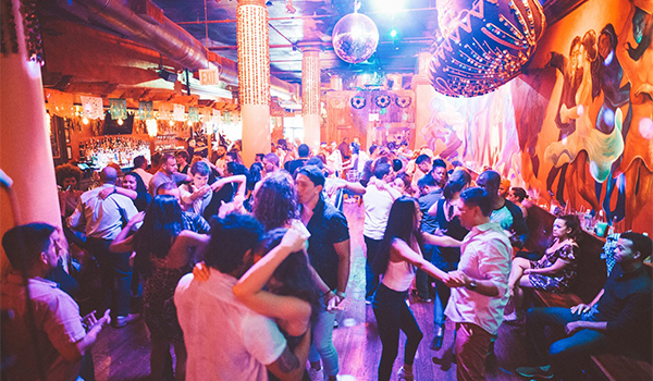 A bright salsa club filled with couples dancing under colourful lights.