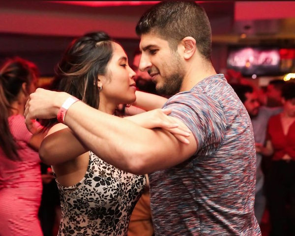 A salsa couple dancing closely under red club lighting.