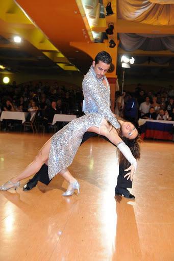 A salsa performance couple dipping on a dance floor in front of an audience.